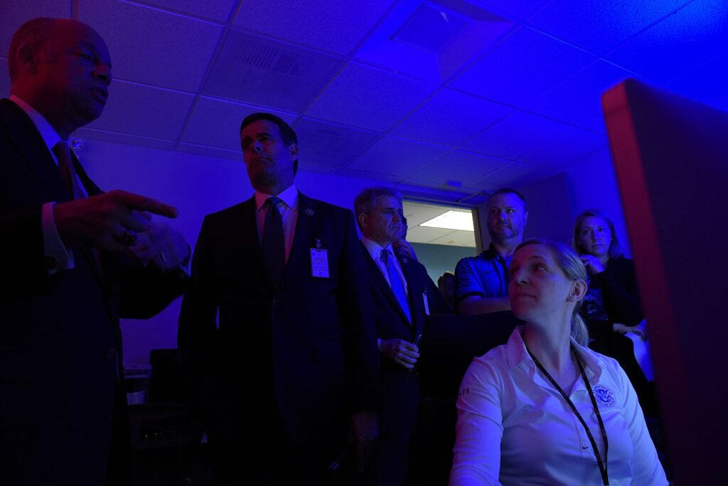 Several government officials stand in front of a computer at a DHS cyber demonstration