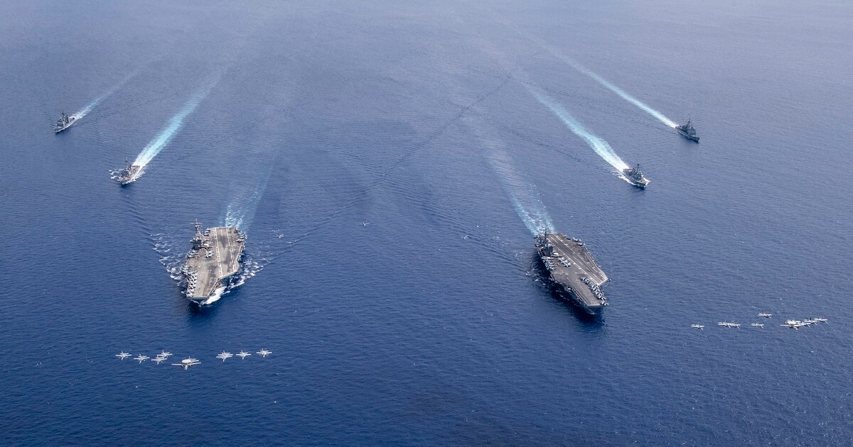 Aircraft from Carrier Air Wings (CVW) 5 and 17 fly in formation over the Nimitz Carrier Strike Force on July 6, 2020, in the South China Sea. The aircraft carriers USS Nimitz (CVN 68), right, and USS Ronald Reagan (CVN 76) and their carrier strike groups are conducting dual carrier operations in the Indo-Pacific as the Nimitz Carrier Strike Force.