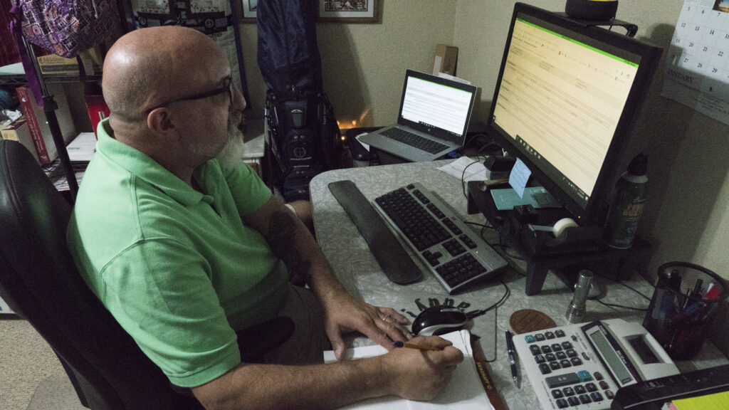 A man works from home with several computers and a calculator.