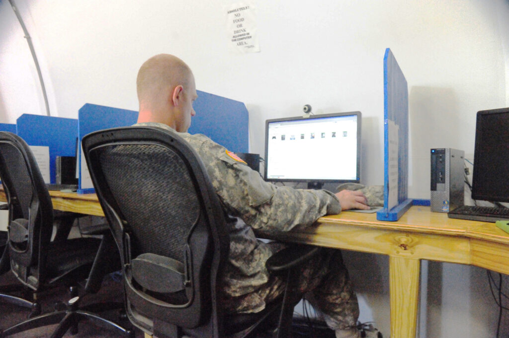 A man in uniform sits in front of a computer with a webcam.
