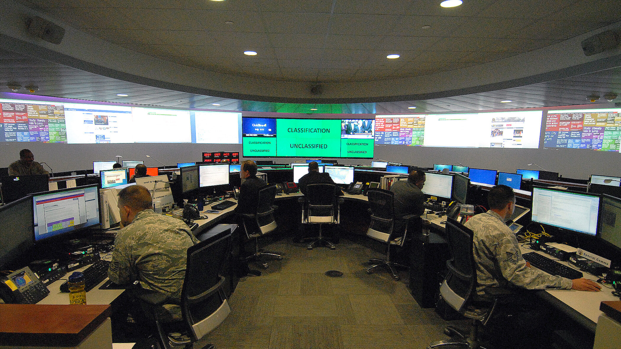 Several people in uniform sit in a room with many computers.